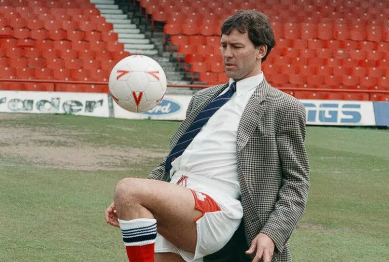 Bryan Robson juggling a ball wearing a suit jacket and tie, but Middlesbroiuh shorts and socks